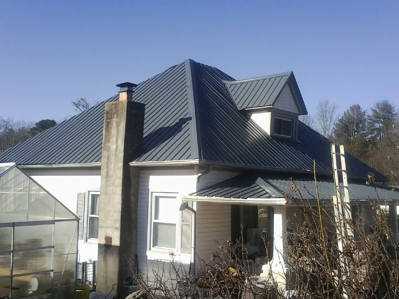 Dark blue standing seam metal roof on a white farmhouse with dormer — Slate & Tile Roof Repair by Roofing Brothers in Williston Park