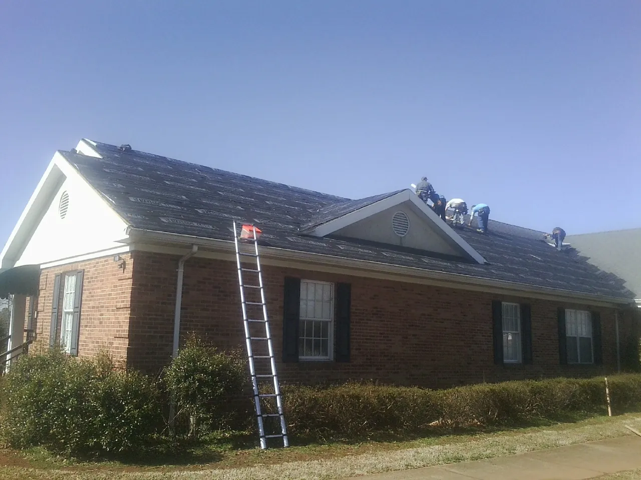 Crew tearing shingles off a brick ranch roof with a ladder set — Emergency Roof Repair work by our crew in Williston Park