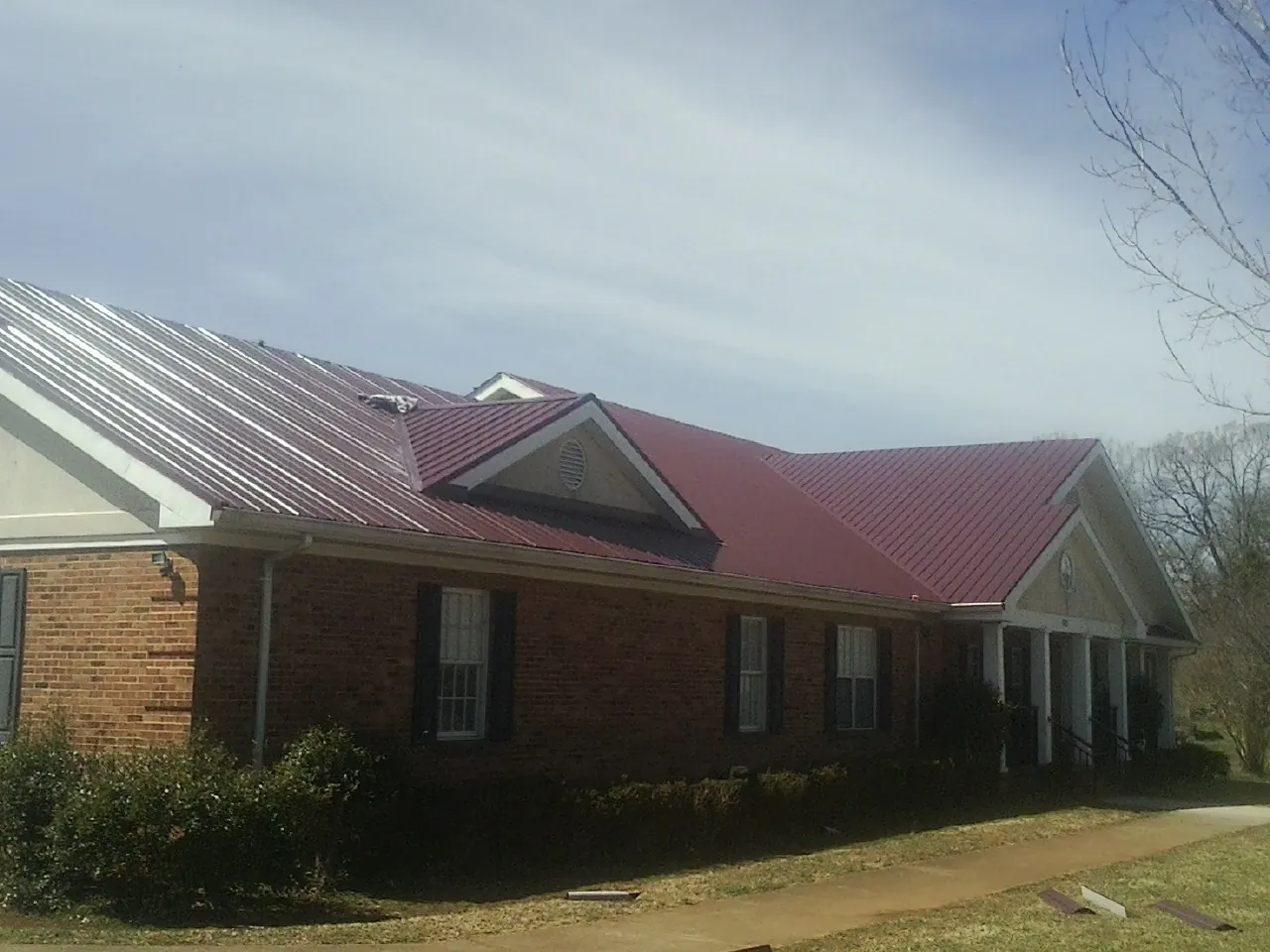 Red metal roof with gabled entries on a long brick building, from a Hail Damage Roof Repair job in Williston Park
