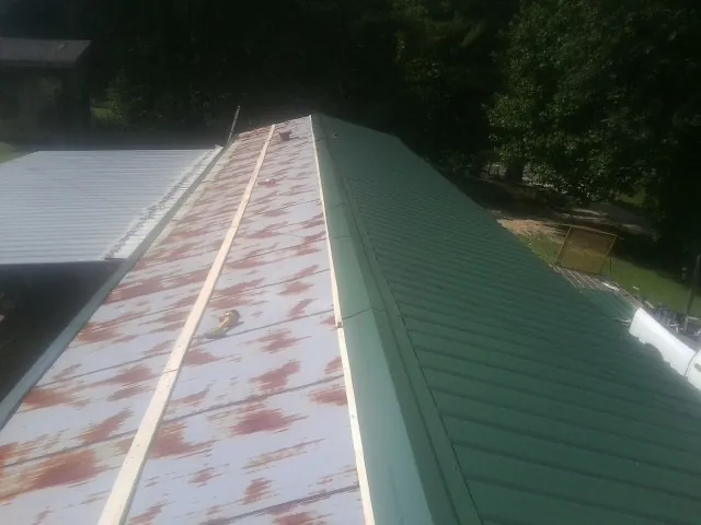 Old rusted panels beside newly installed green metal roofing — Wind Damage Roof Repair by Roofing Brothers in Williston Park