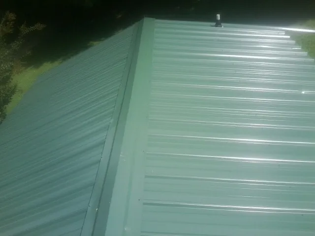 New green metal panels meeting at the ridge of a roof — Flat Roof Repair work by our crew in Williston Park