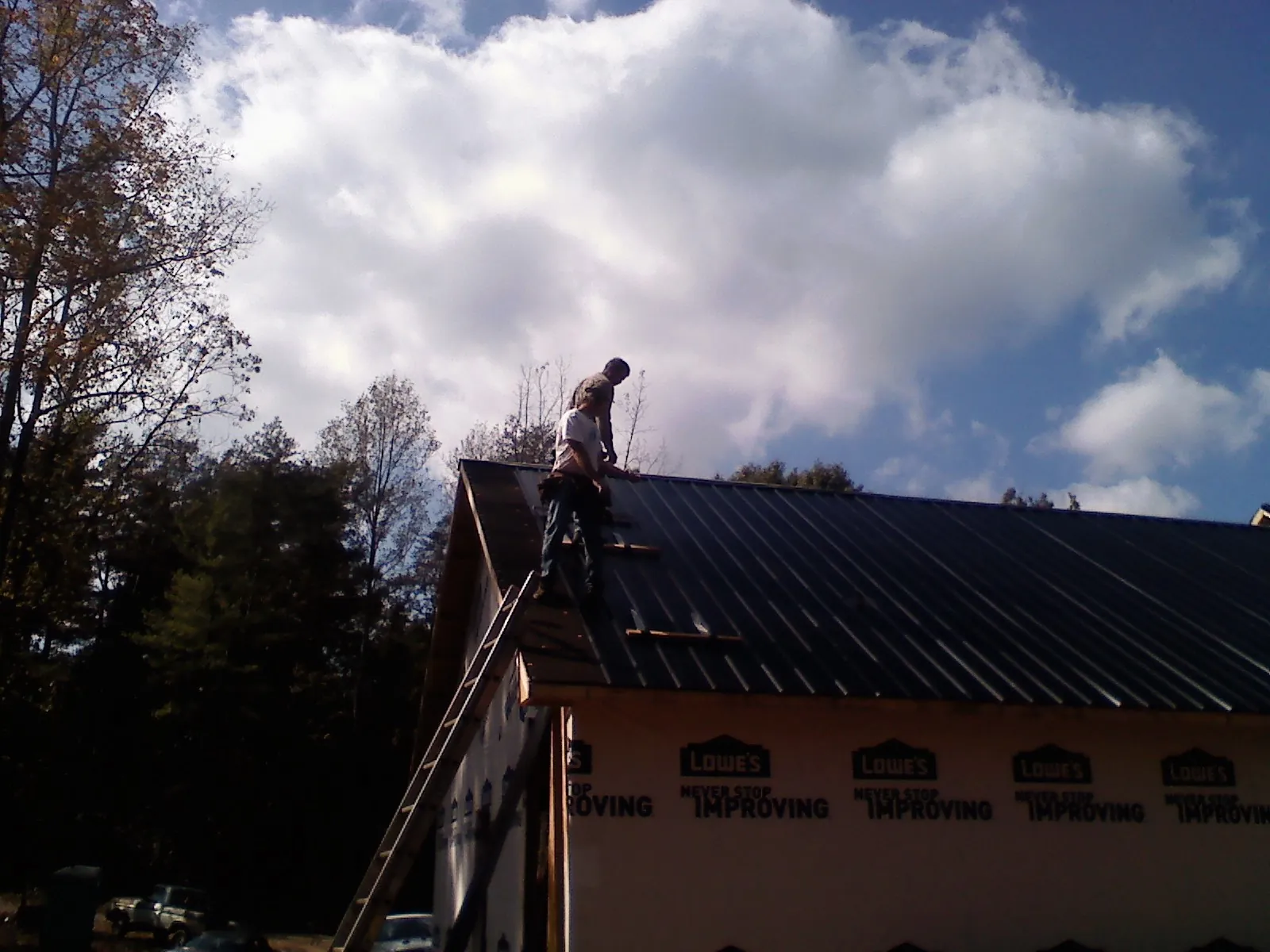 Roofer fastening dark metal panels high against a cloudy sky, from a Roof Inspection job in Williston Park