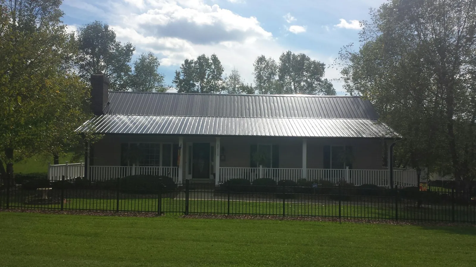 Gray metal roof on a brick ranch with a full width front porch — Gutter Guard Installation work by our crew in Williston Park