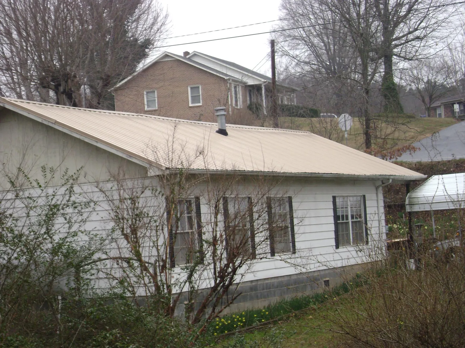 Tan metal roof on a white sided house set into a hillside — Commercial Roofing by Roofing Brothers in Williston Park